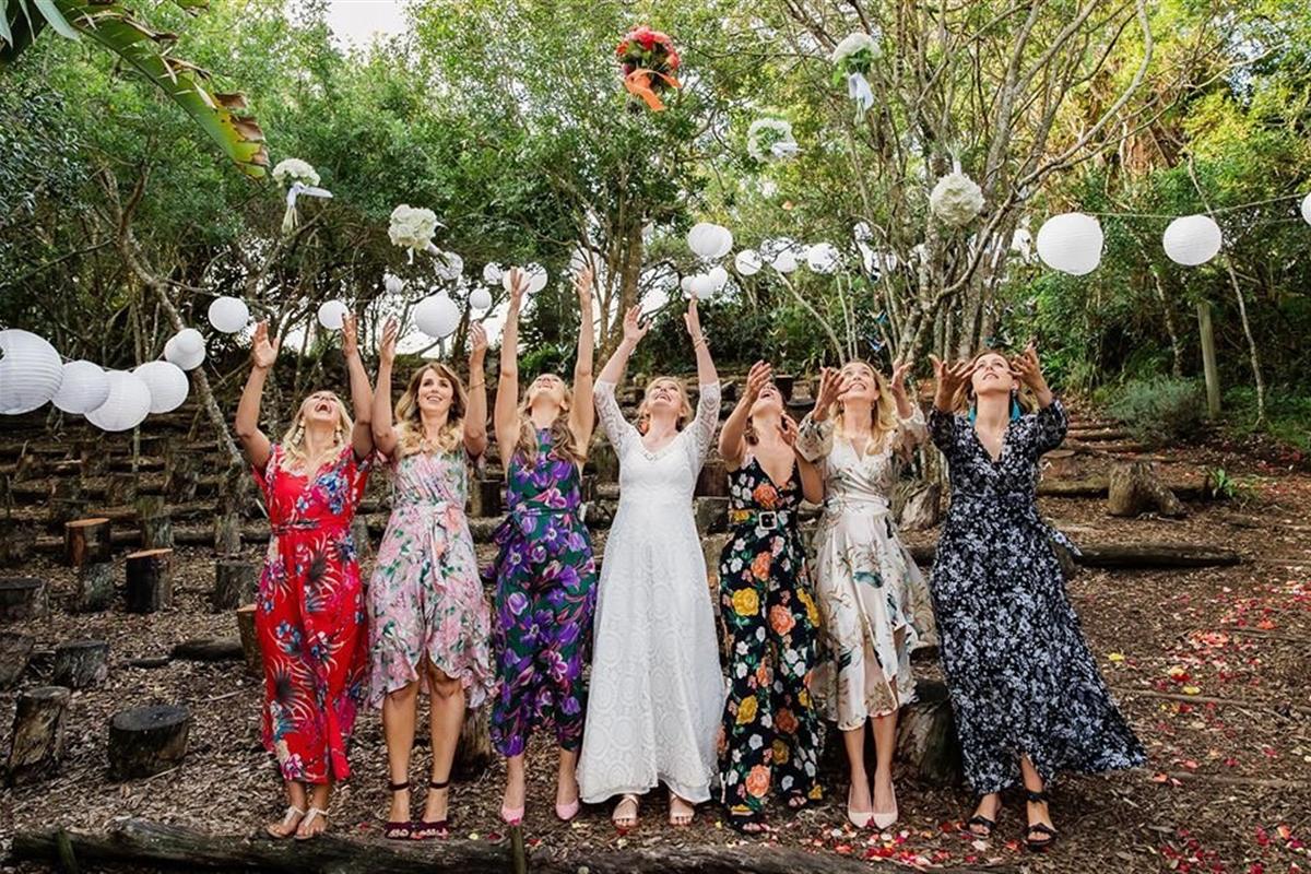 Bridesmaids and a bride throwing bouquets in the air in the forest theatre, with white paper lanterns strung between the trees.
